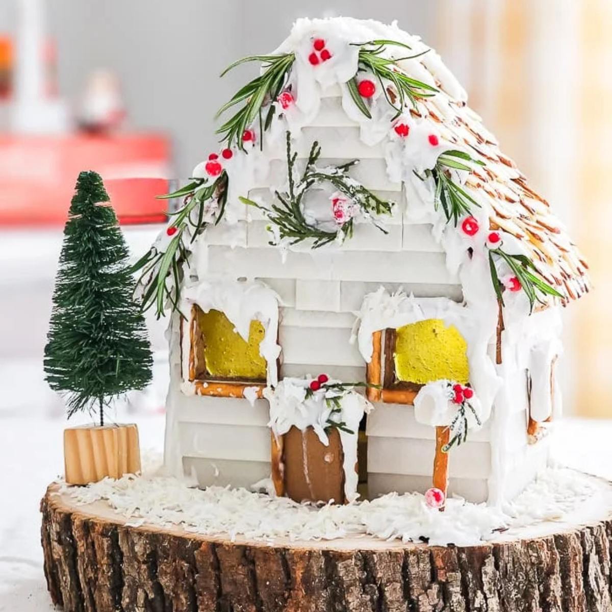 A whimsical gingerbread house adorned with rosemary sprigs, white icing, and red candies, resembling a winter cabin.