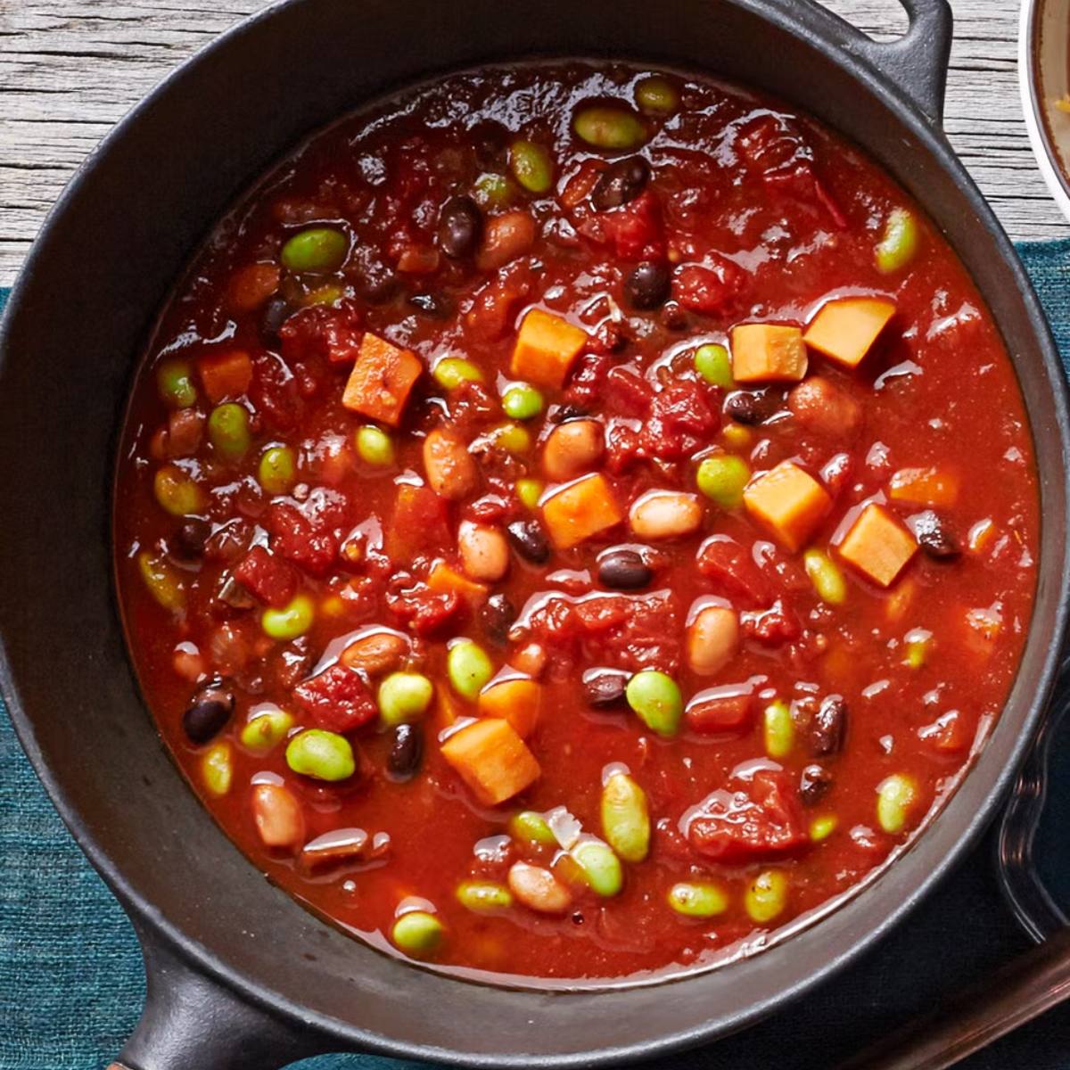 A pot of chili filled with various beans, sweet potatoes, and vegetables, simmering in a rich tomato broth.