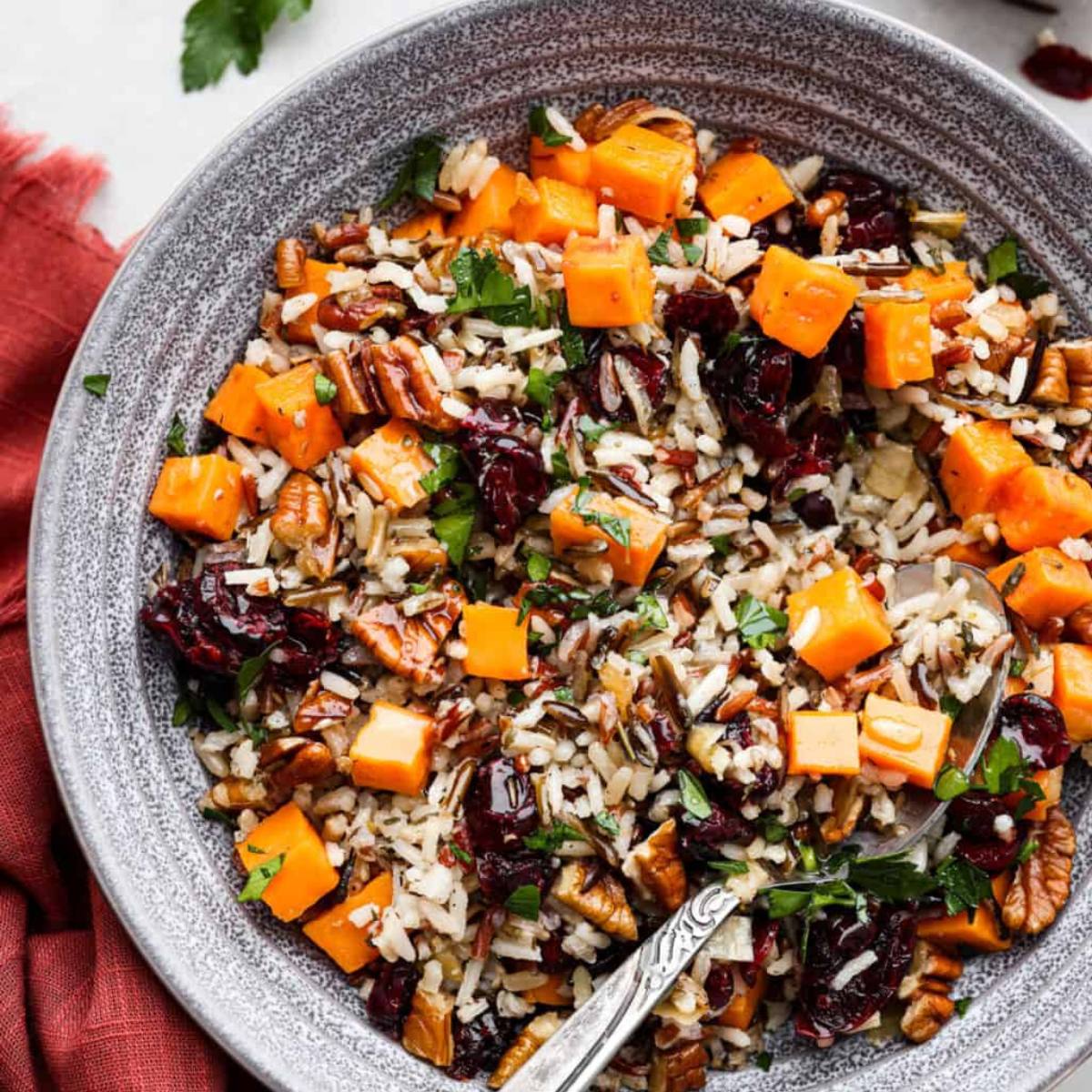 A bowl of festive wild rice pilaf with roasted sweet potatoes, cranberries, pecans, and fresh herbs.