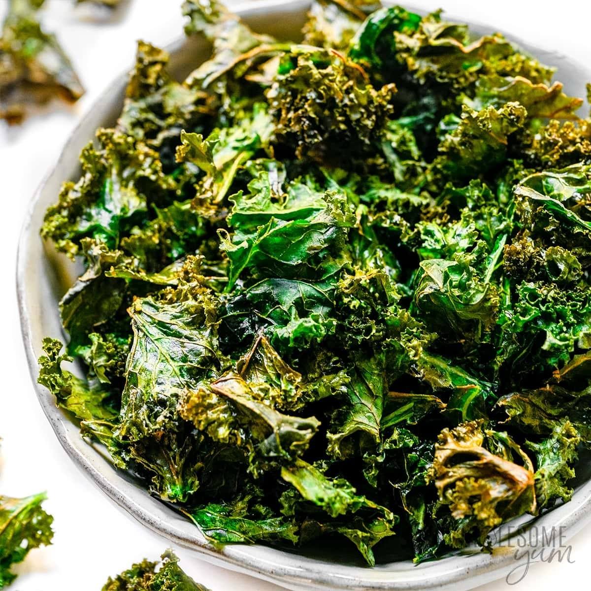 A bowl of crispy, air fried kale chips. The kale chips are a vibrant green color and look light and airy.