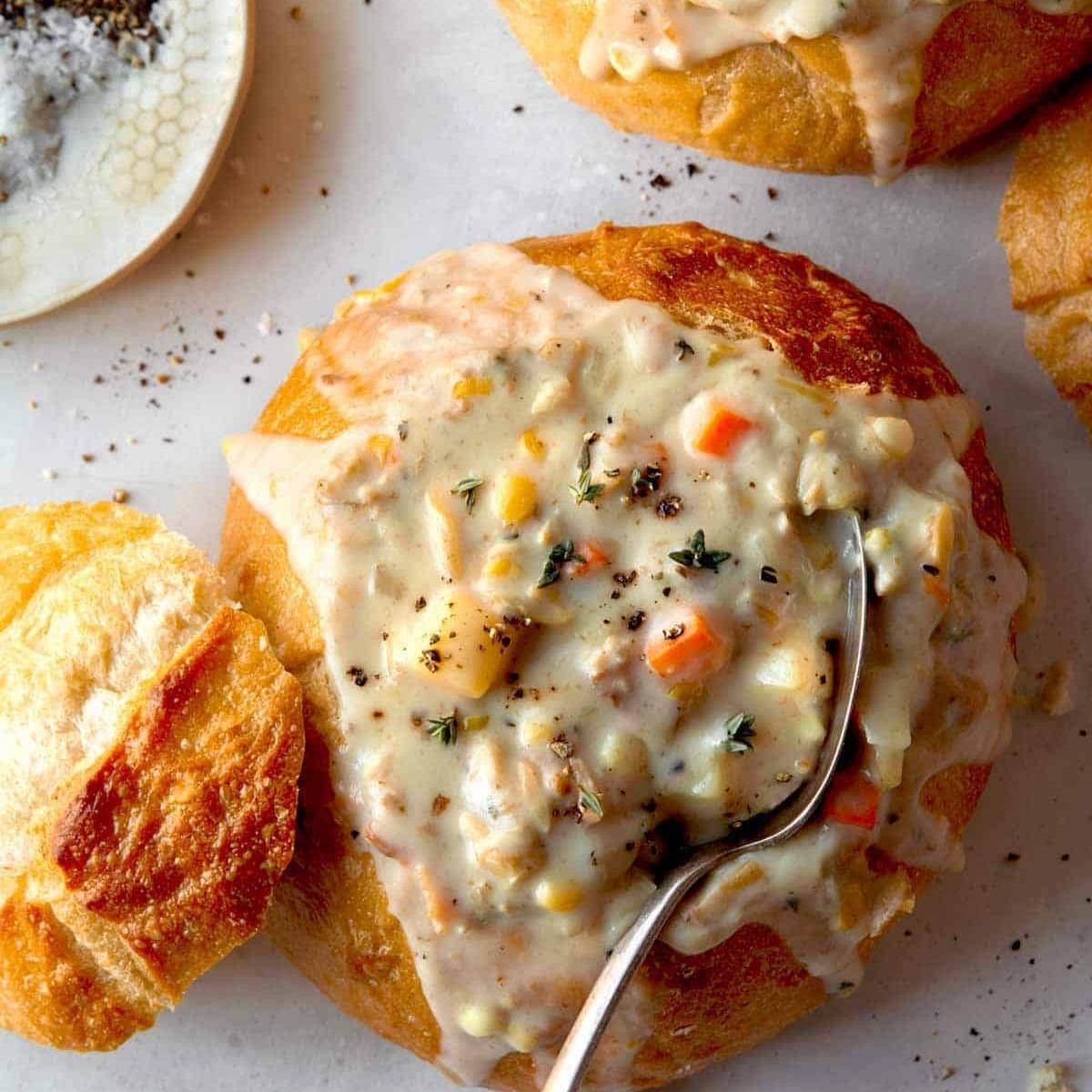 A bowl of creamy clam chowder served in a hollowed-out bread bowl.