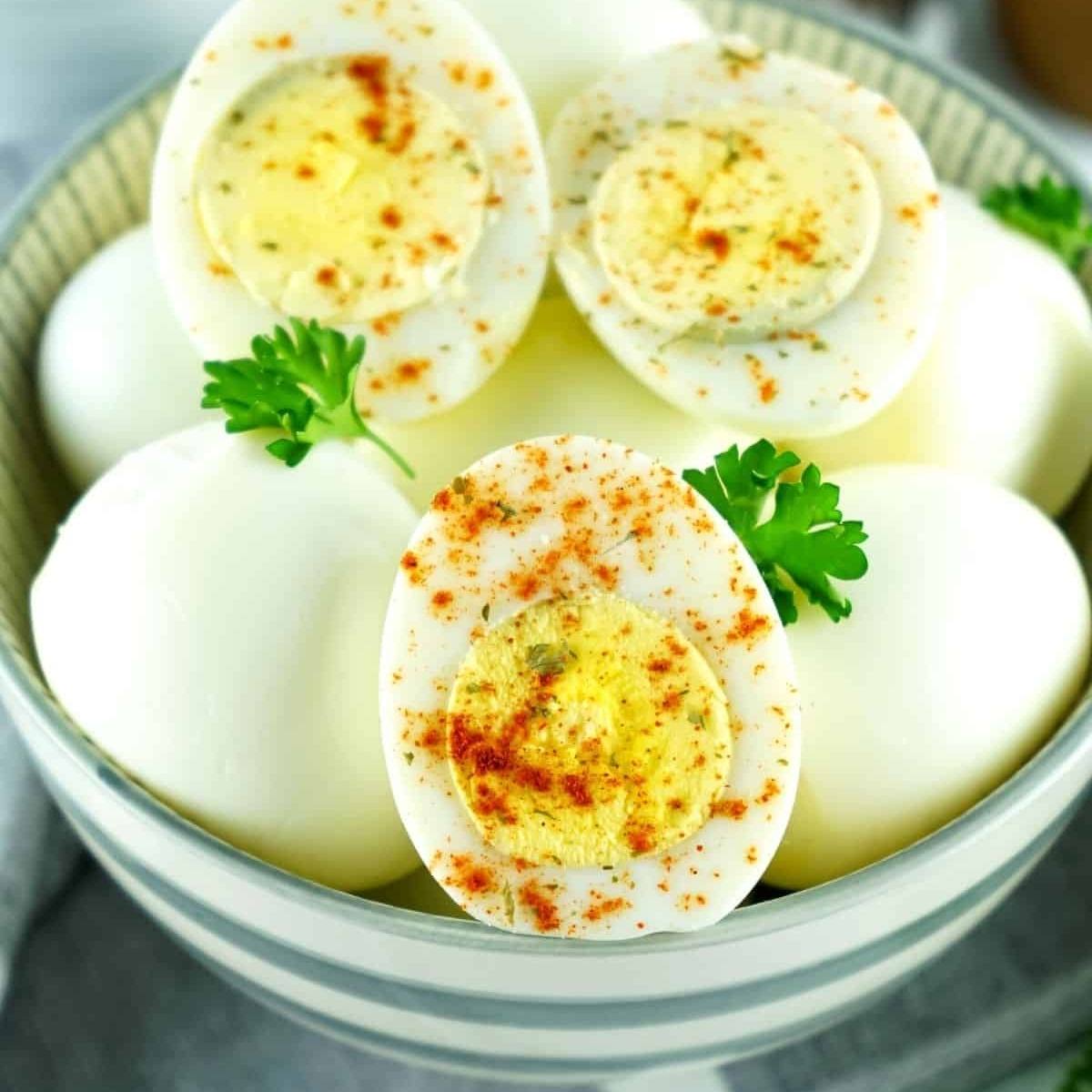 A bowl of hard-boiled eggs with one egg cut in half and sprinkled with paprika and parsley.