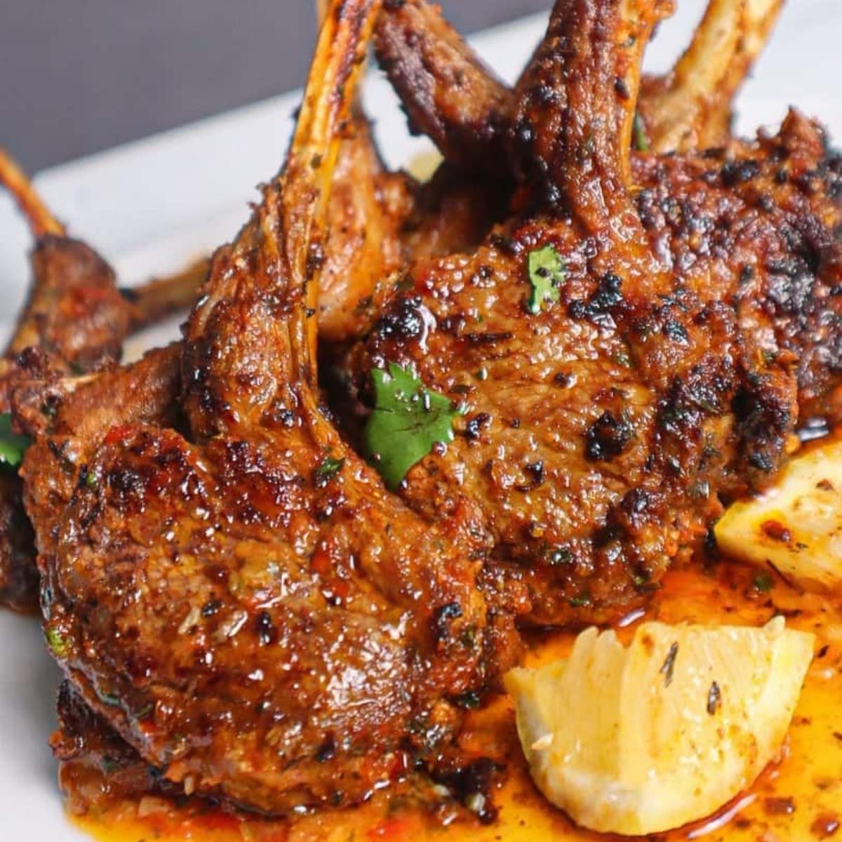 A plate of juicy, grilled lamb chops with a lemon wedge. 