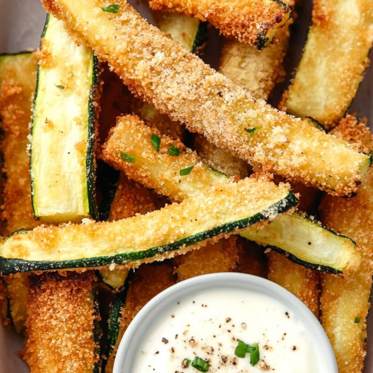 A plate of crispy air fried zucchini fries with a side of dipping sauce. The zucchini fries are golden brown and look delicious!