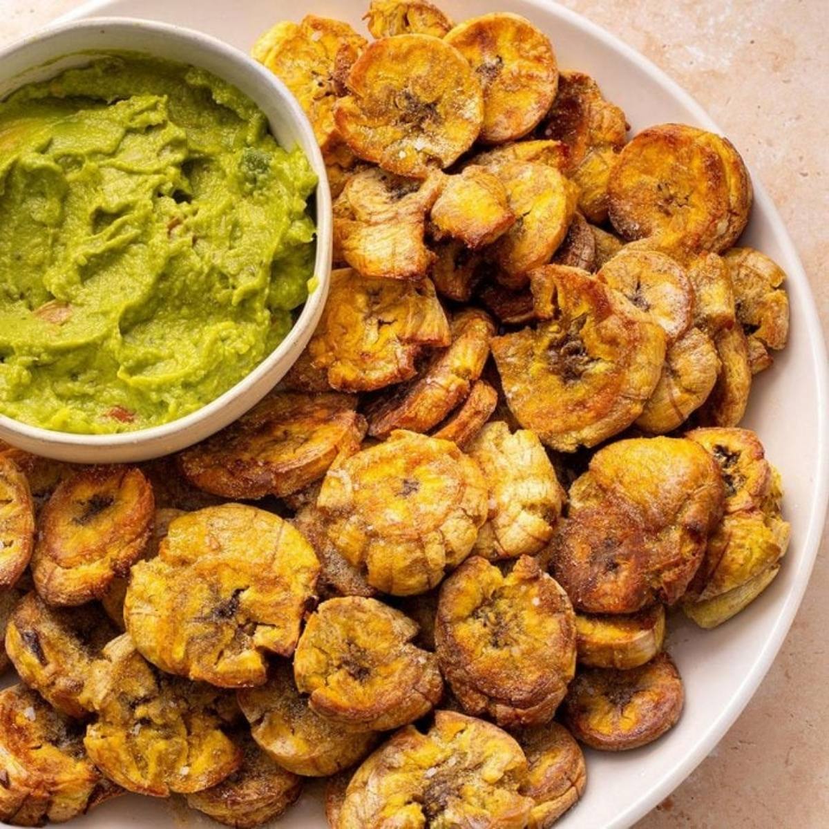 A plate of crispy, golden-brown plantain chips with a bowl of guacamole. The plantain chips look delicious and perfect for dipping.