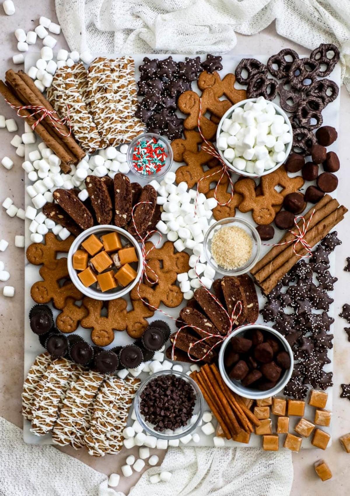 The board includes gingerbread men cookies, chocolate chip cookies, pretzels, marshmallows, chocolate chips, caramel candies, biscotti, and sprinkles.