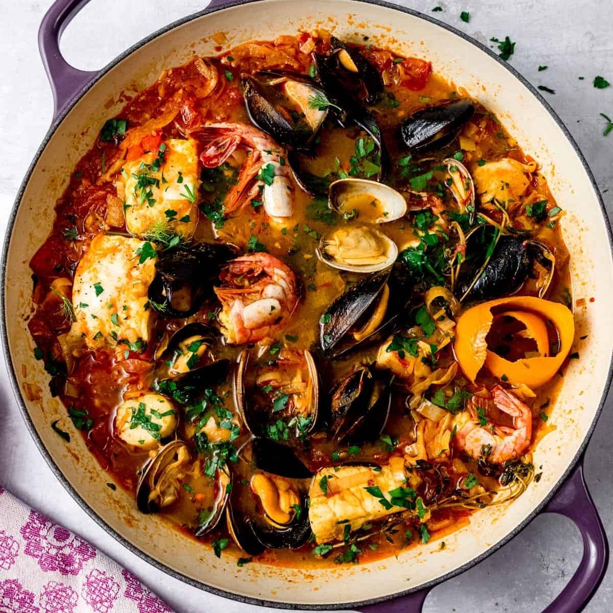 A vibrant seafood stew simmering in a pot. It's brimming with fresh fish, plump mussels, juicy shrimp, and clams, all swimming in a rich tomato-based broth. 