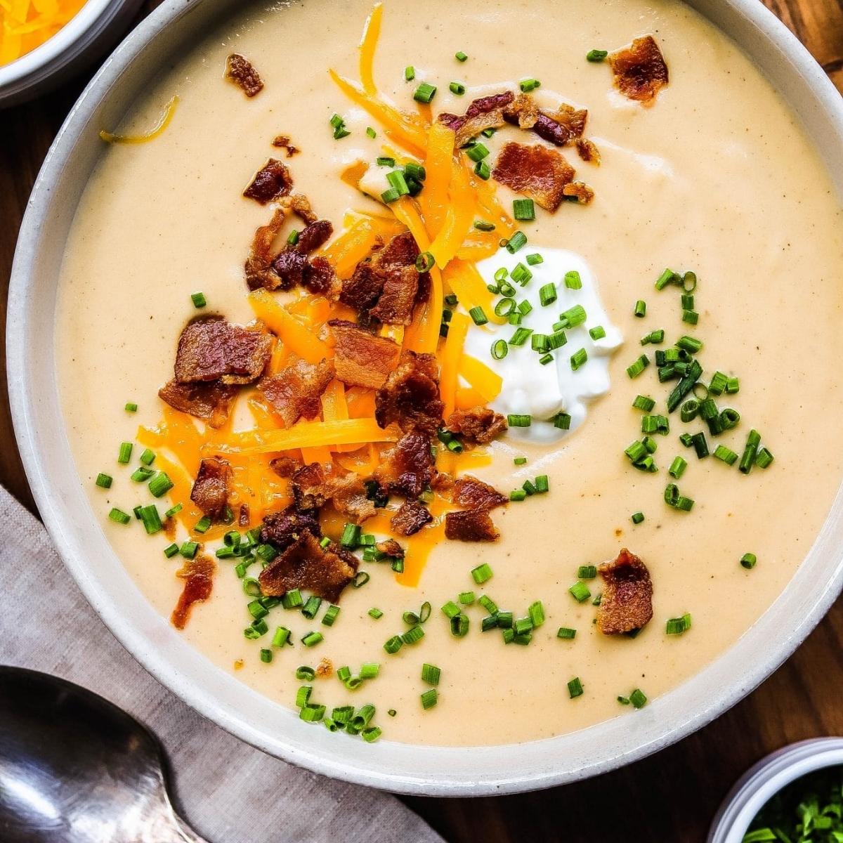 A bowl of creamy potato soup topped with shredded cheddar cheese, crumbled bacon bits, chives, and a dollop of sour cream.