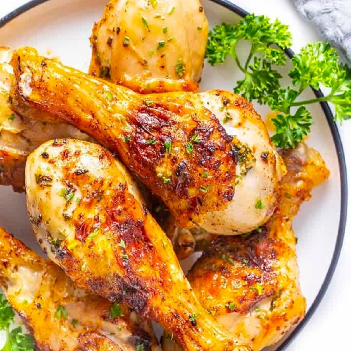 A plate of golden-brown, air fried chicken legs. The chicken legs are seasoned and cooked to perfection, with a crispy skin and juicy meat. They are garnished with fresh parsley.