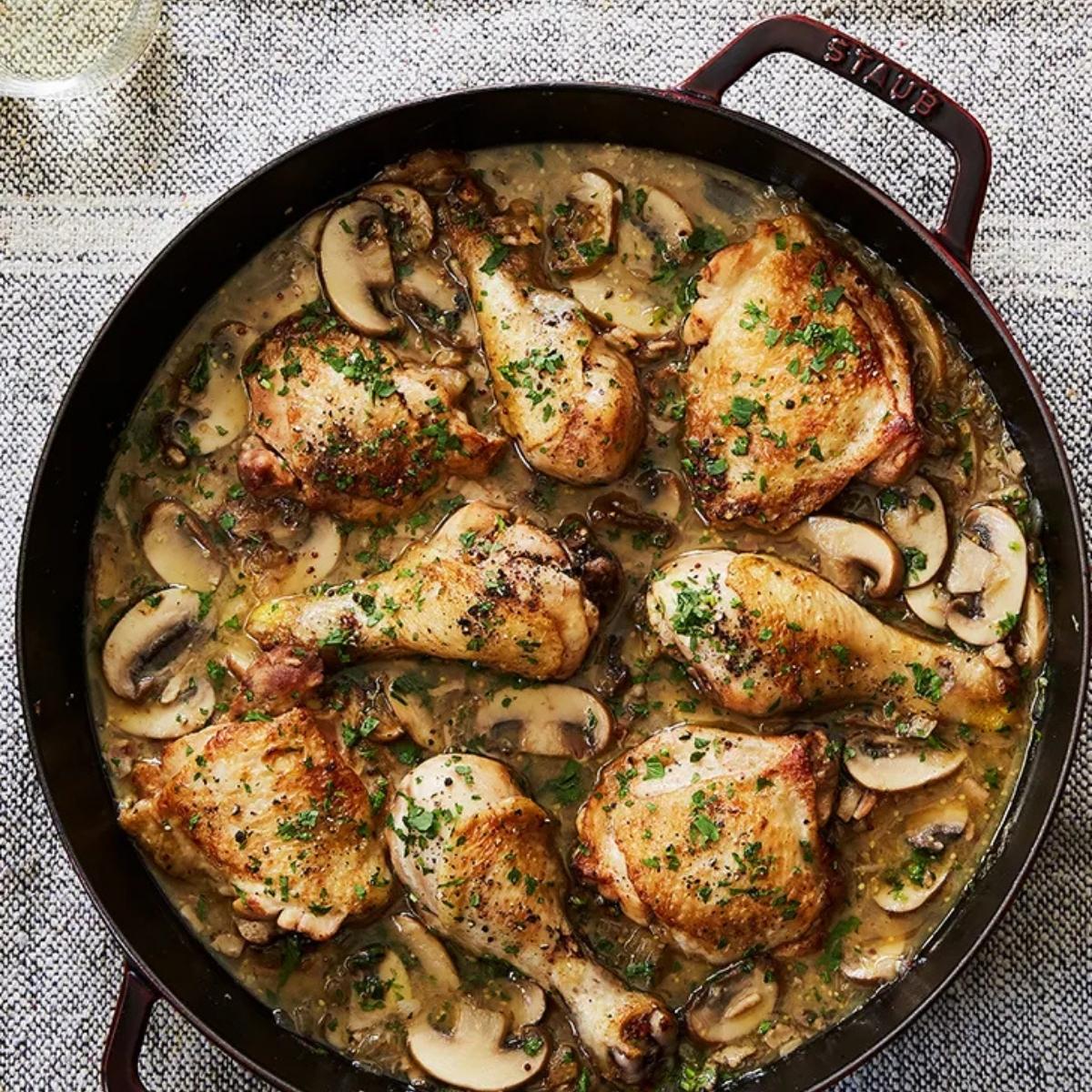 A skillet filled with a mouthwatering chicken dish. The chicken pieces are cooked to a golden brown and are nestled in a rich, creamy sauce filled with mushrooms.