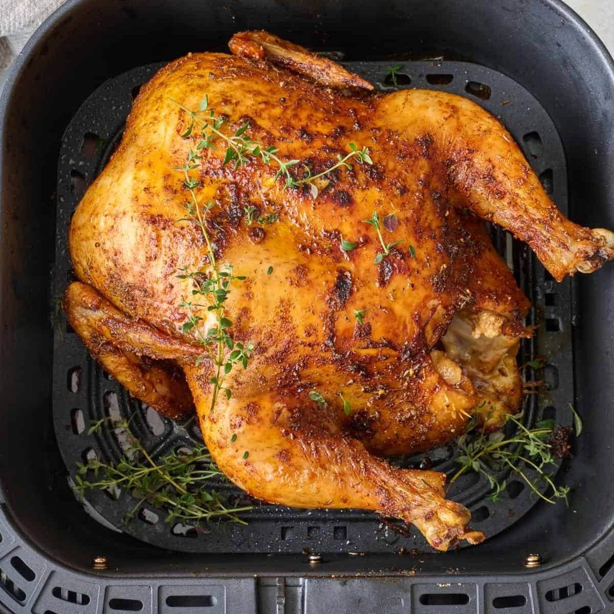 A golden-brown, whole air fryed chicken cooking in an air fryer basket. The chicken is seasoned with herbs and looks crispy and delicious.