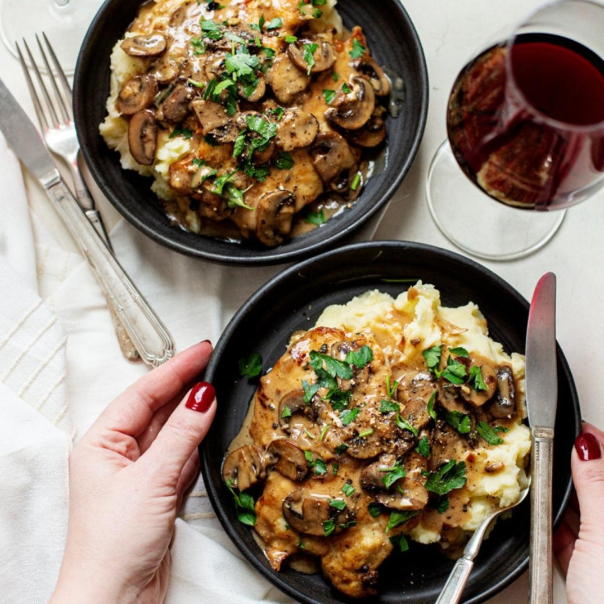 A top-down view of two plates of Chicken Marsala. Each plate holds a chicken breast covered in a rich, creamy mushroom sauce and served over a bed of mashed potatoes.