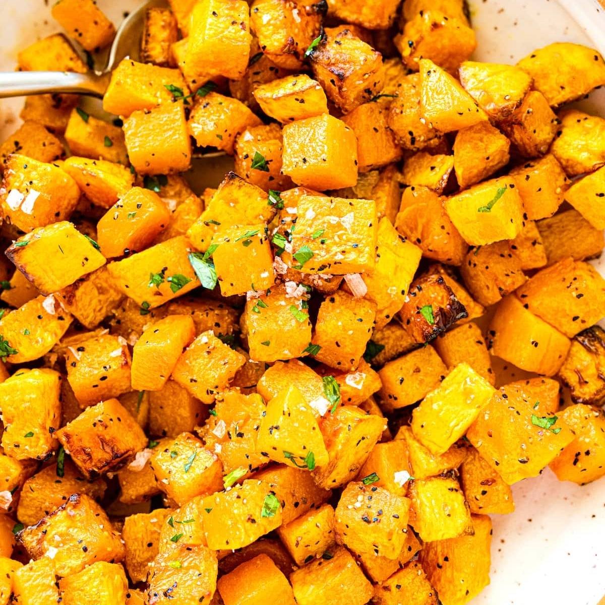 A bowl of air fried butternut squash cubes. The squash is golden brown and sprinkled with salt and parsley.