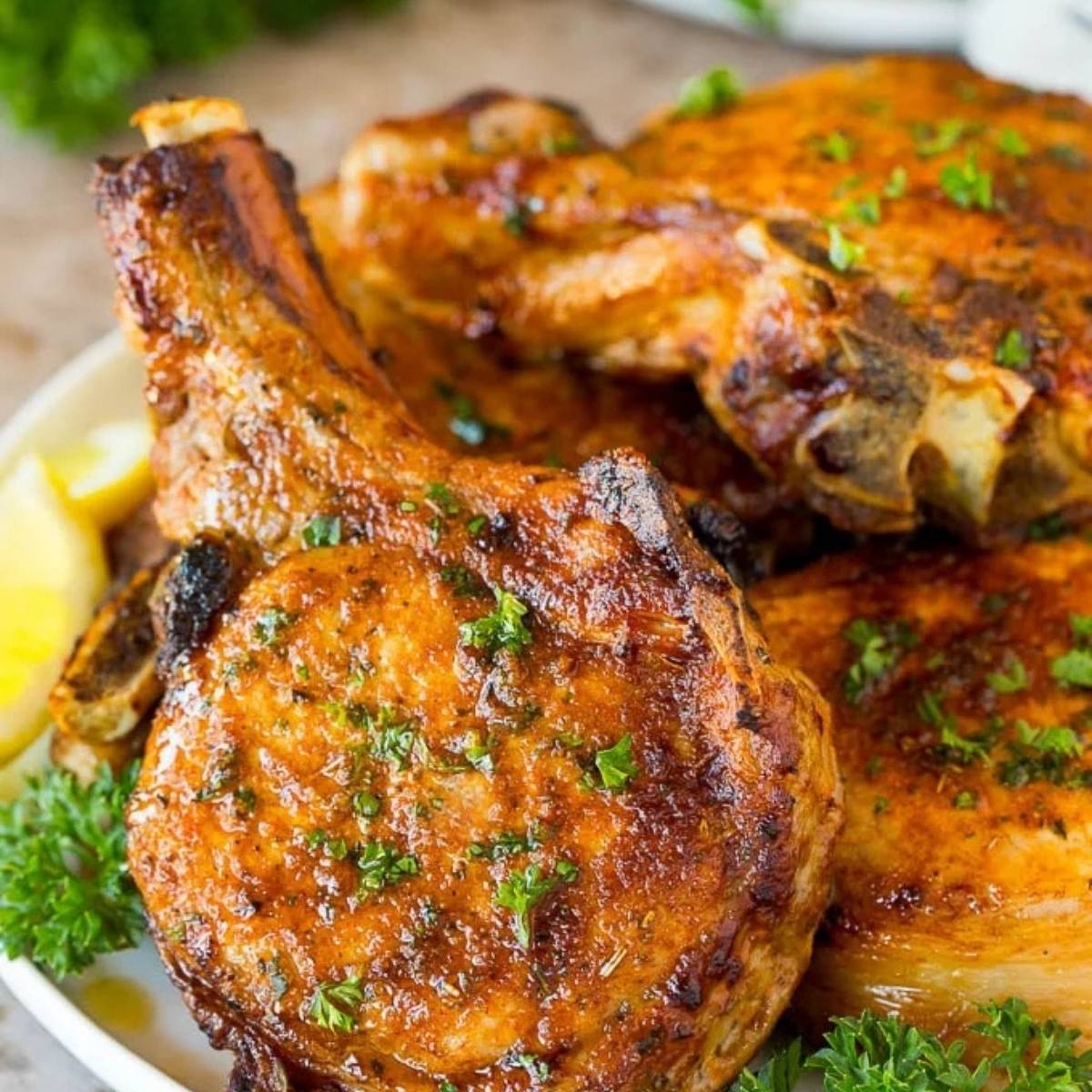 This image shows a plate of air fried pork chops. They have a beautiful golden-brown crust and are garnished with fresh parsley and lemon wedges.