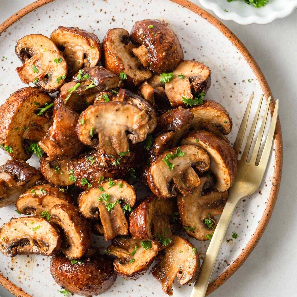 A plate of golden-brown air fried mushrooms. The mushrooms look tender and juicy, and they are sprinkled with fresh parsley. A fork is resting on the plate.