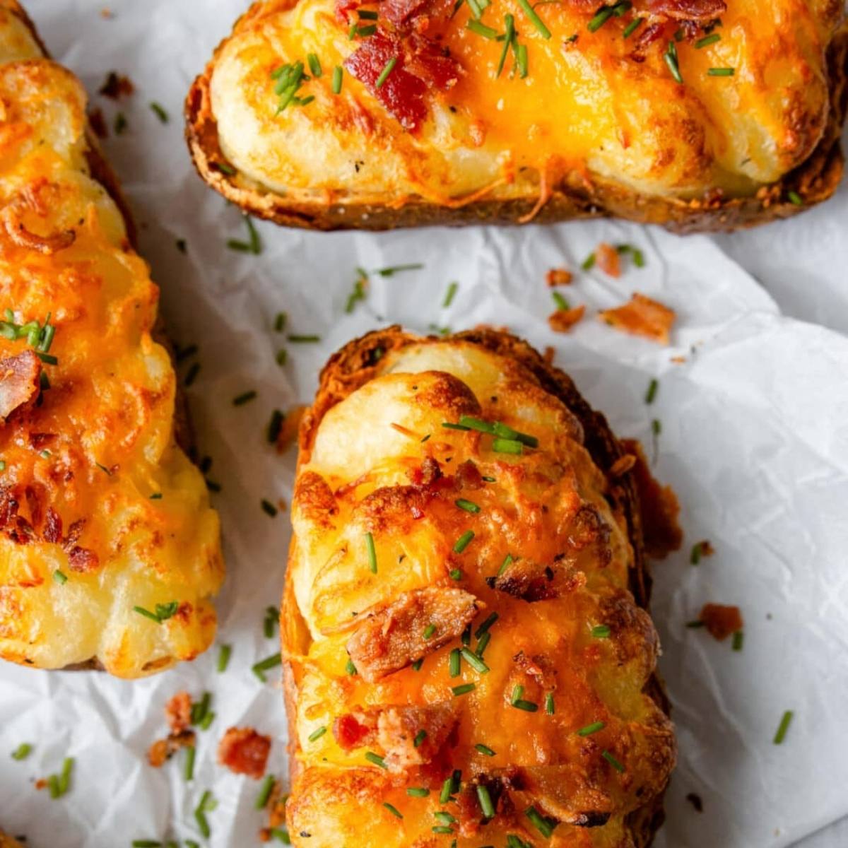 A close-up of loaded air fried potatoes. The potatoes are topped with melted cheese, crumbled bacon bits, and chives. They look delicious and cheesy!