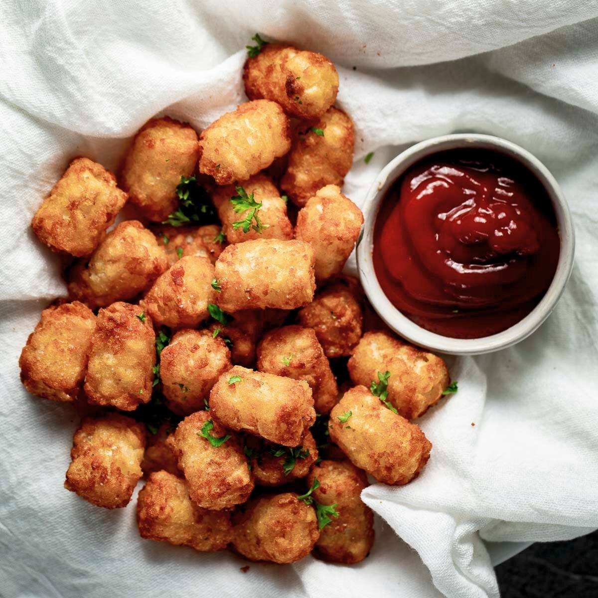 A basket of crispy, golden-brown tater tots served with a small bowl of ketchup. The tots look delicious and perfect for dipping!