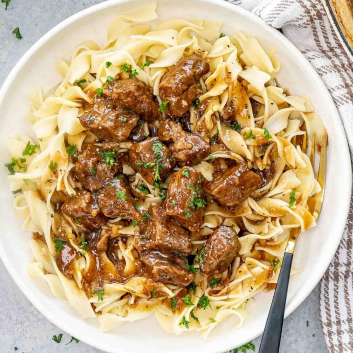 A bowl of hearty beef stew served over egg noodles. The stew is rich and flavorful, with tender chunks of beef in a savory gravy.