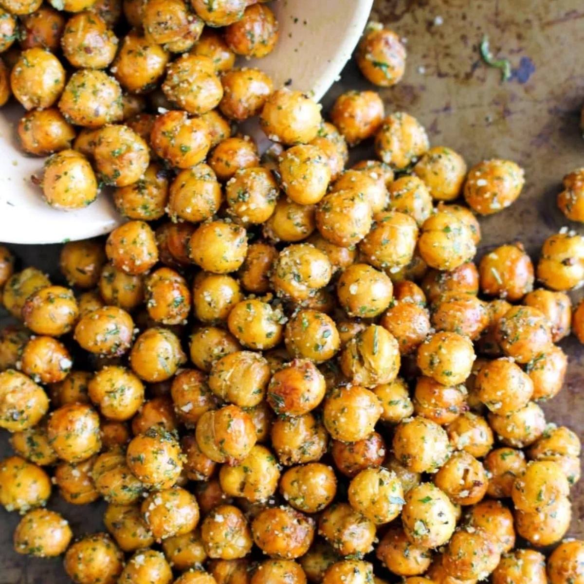 A bowl of crispy, air fried chickpeas spilling onto a baking sheet. The chickpeas are golden brown and seasoned with herbs and spices. They look like a delicious and healthy snack!