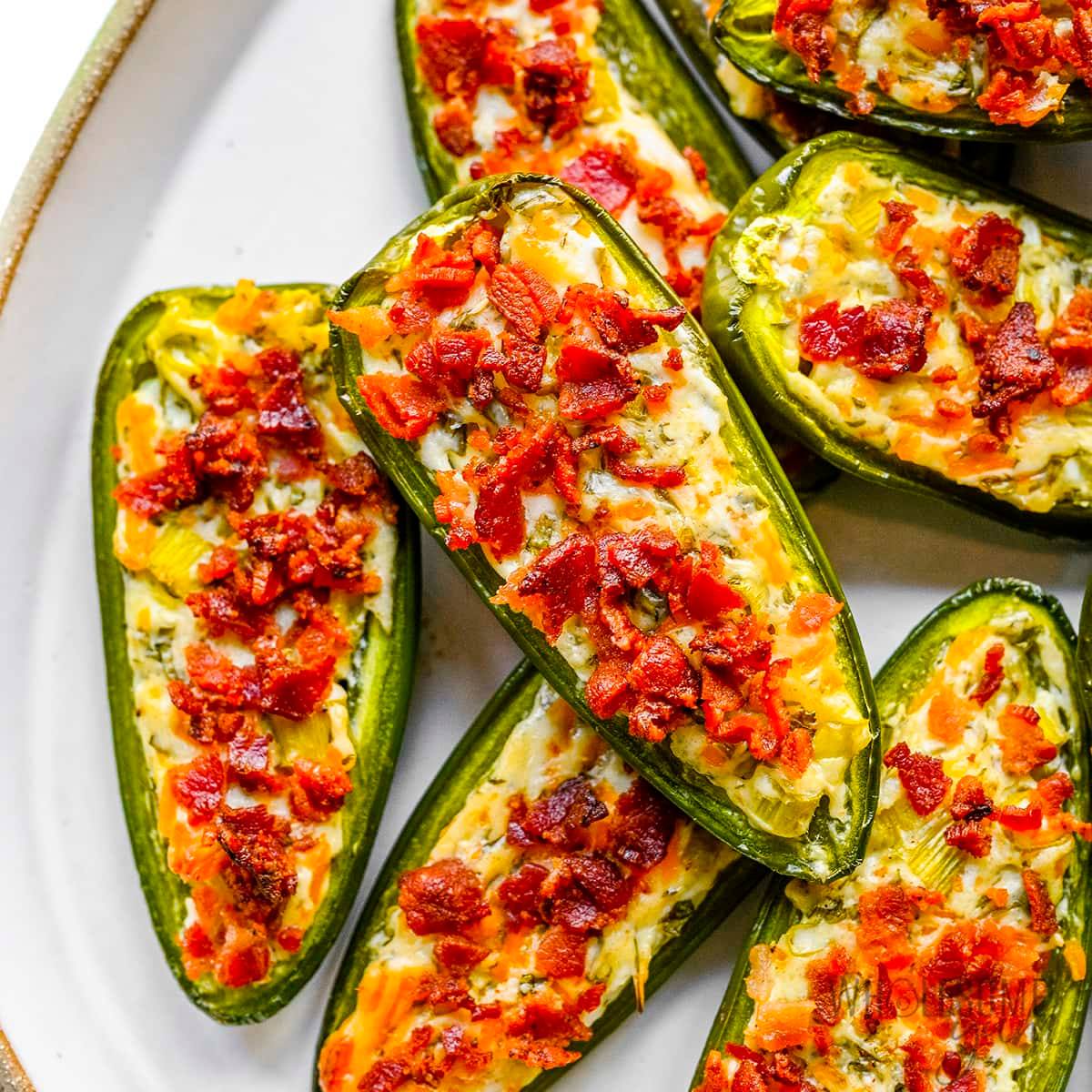 A plate of baked jalapeño peppers stuffed with a creamy cheese mixture and topped with crispy bacon bits.