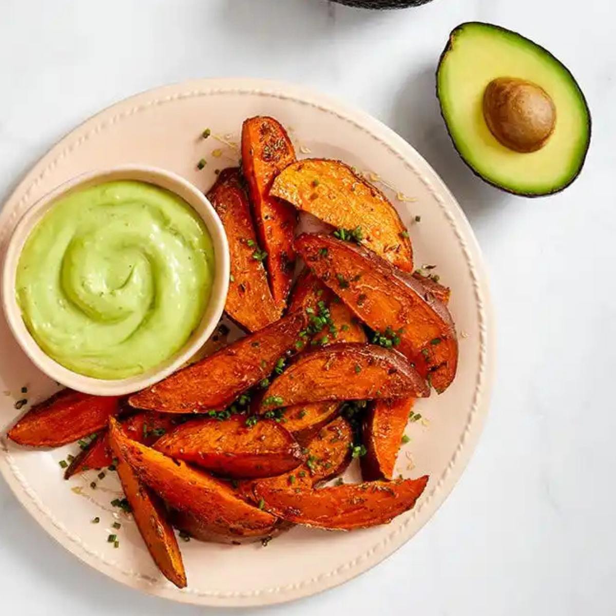 A plate of crispy, golden-brown sweet potato wedges served with a side of avocado dip.