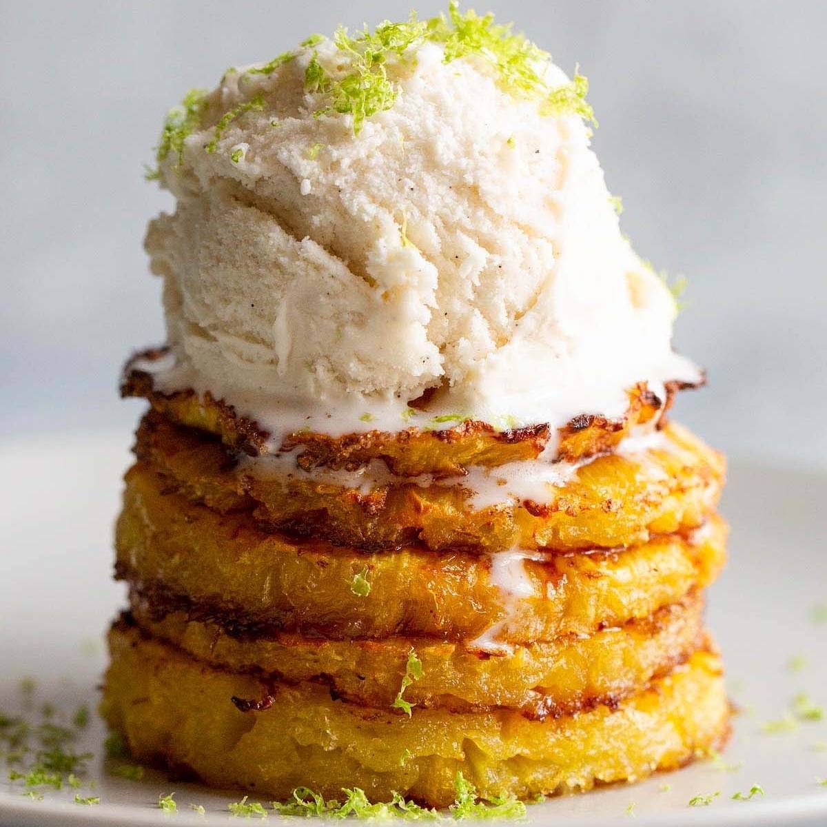 A delicious dessert of air fried pineapple rings topped with a scoop of vanilla ice cream. The pineapple rings are caramelized and sprinkled with lime zest. It looks refreshing and perfect for a warm day.