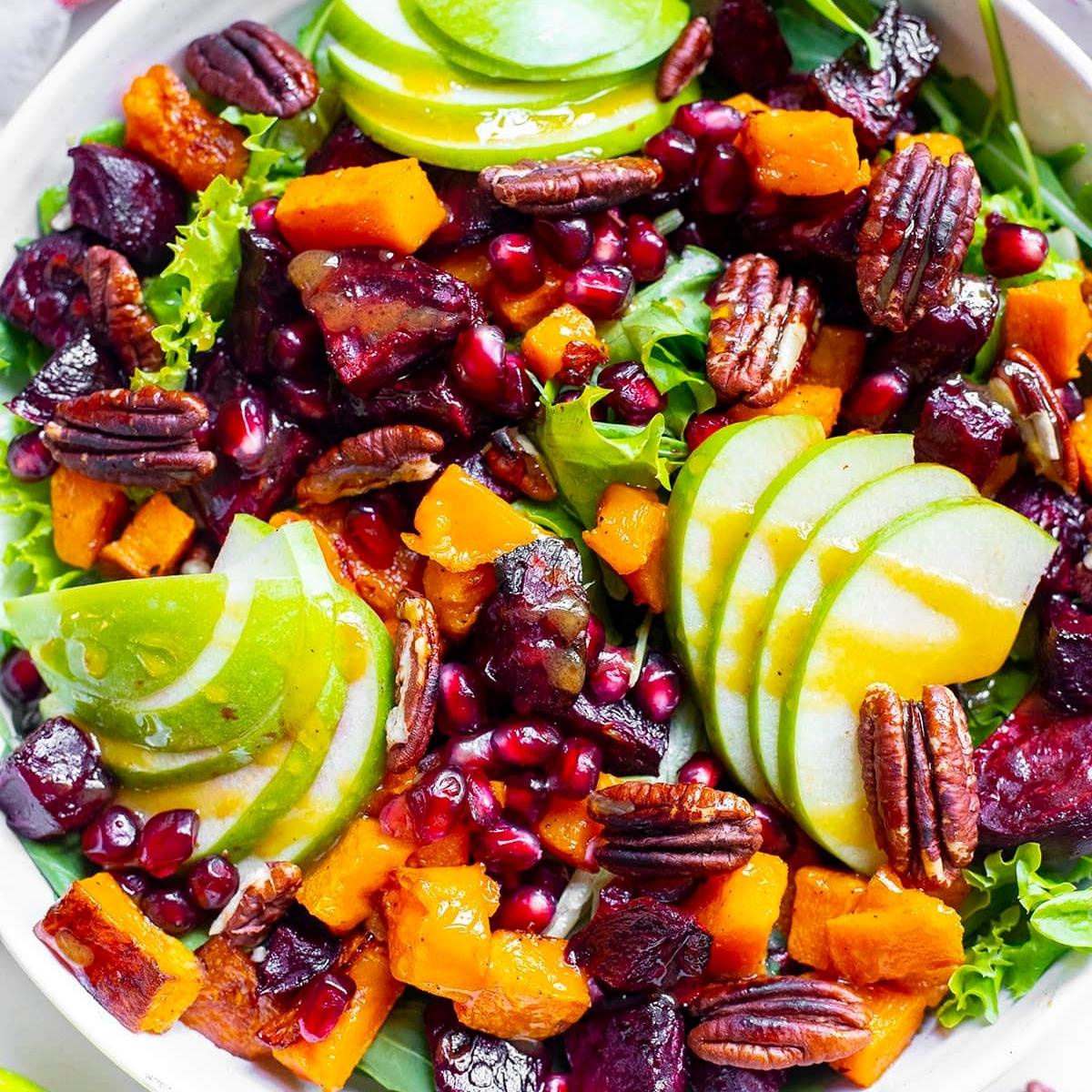 A vibrant and colorful salad with roasted beets, butternut squash, apples, pomegranate seeds, pecans, and a drizzle of honey vinaigrette.