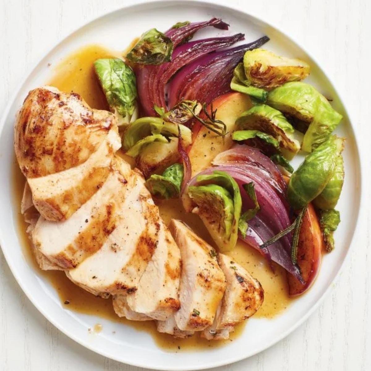 A plate of sliced roasted chicken breast served with a medley of roasted vegetables.