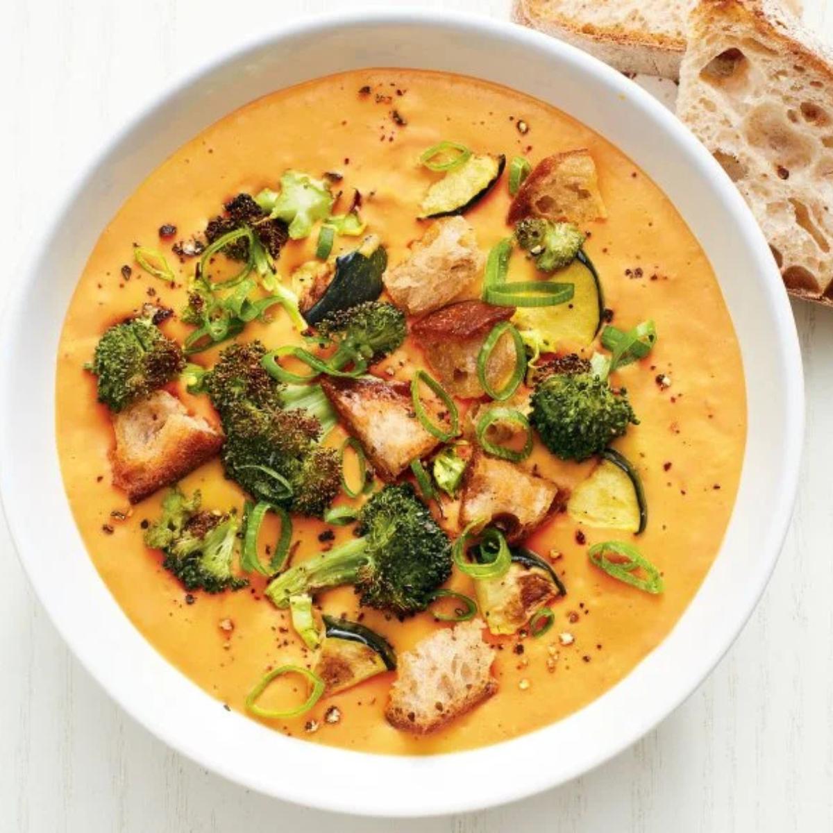 A bowl of creamy butternut squash soup garnished with roasted broccoli florets, croutons, and sliced green onions.