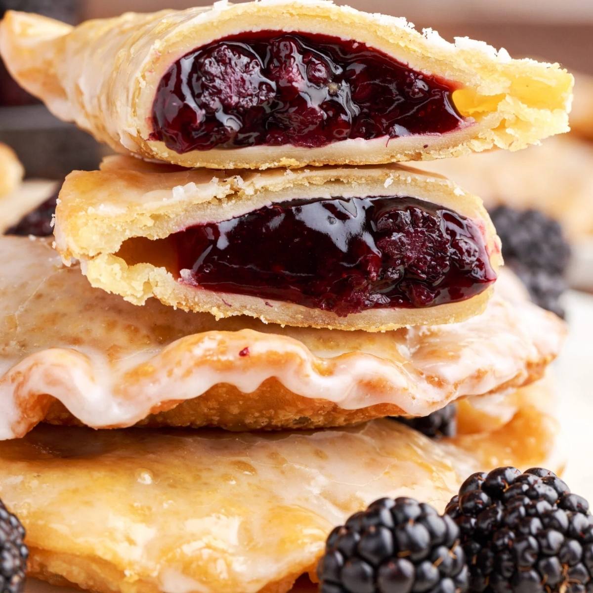 A stack of golden-brown blackberry hand pies. The pies are cut in half, revealing a sweet and juicy filling. They are dusted with powdered sugar and look absolutely delicious!







