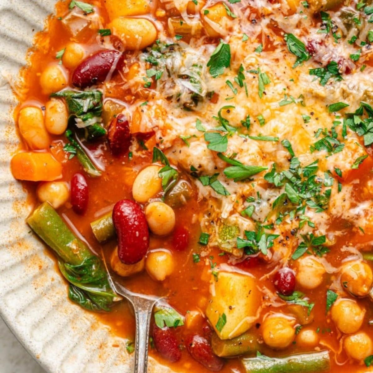 A bowl of hearty Minestrone soup, brimming with vegetables like carrots, beans, and zucchini, and topped with grated cheese and fresh parsley.