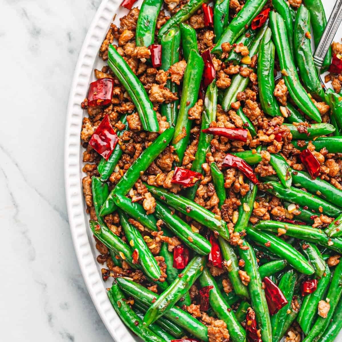 A plate of stir-fried green beans with ground pork and chili peppers.