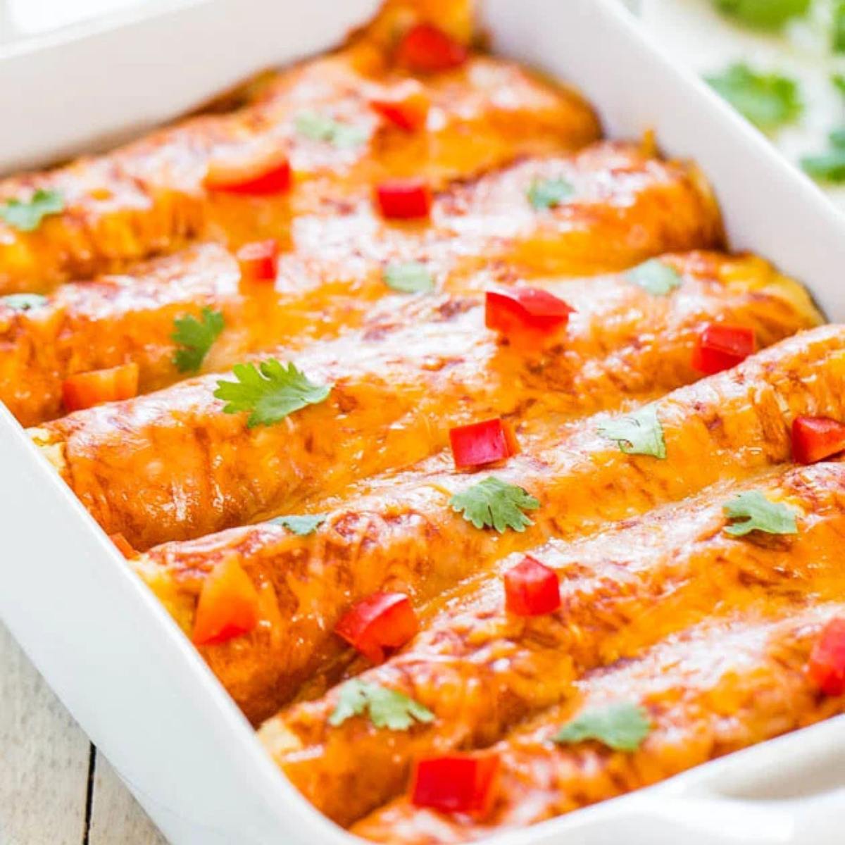 A baking dish filled with enchiladas topped with melted cheese, red pepper flakes, and cilantro.