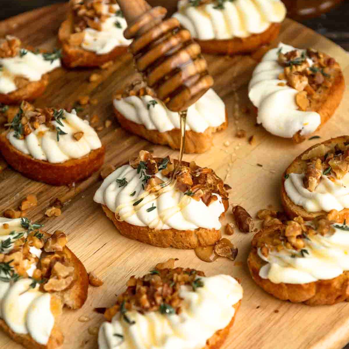 A wooden board filled with toasted bread topped with whipped ricotta, walnuts, honey, and fresh thyme.