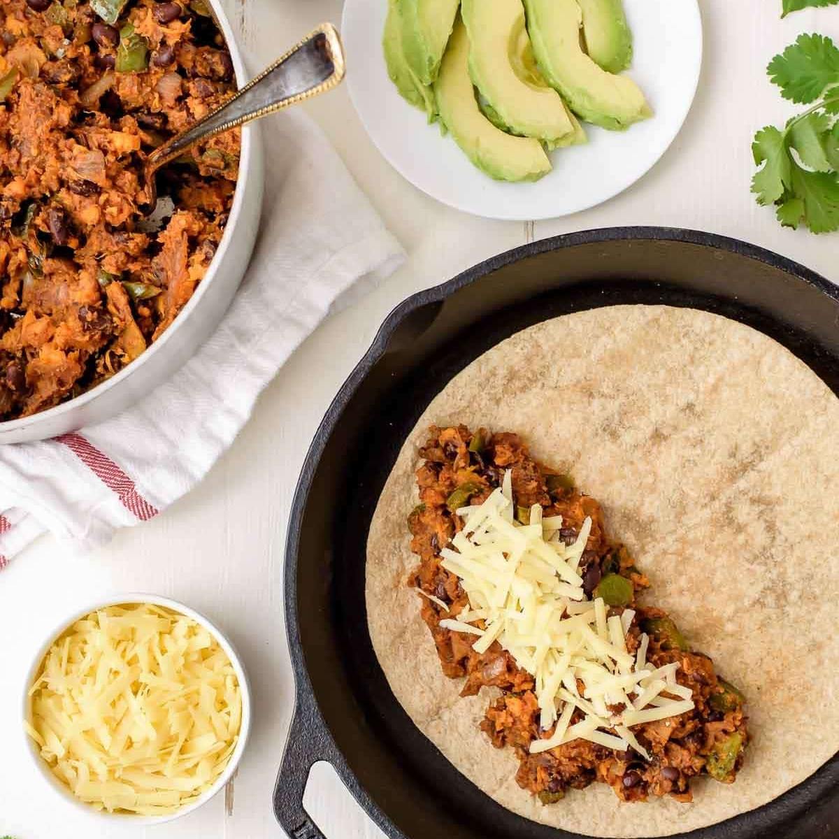 A skillet with a tortilla filled with a mixture of sweet potatoes, black beans, and cheese.