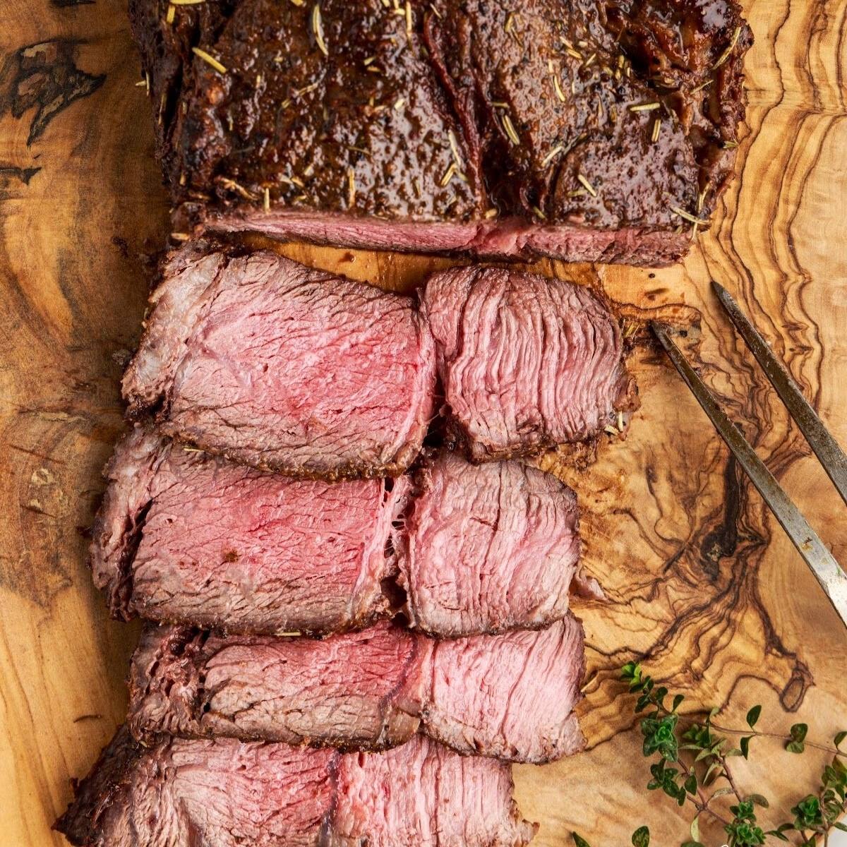 The meat looks tender and juicy, with a rich brown crust. It's likely seasoned with herbs and spices, as there are sprigs of rosemary visible on the cutting board.