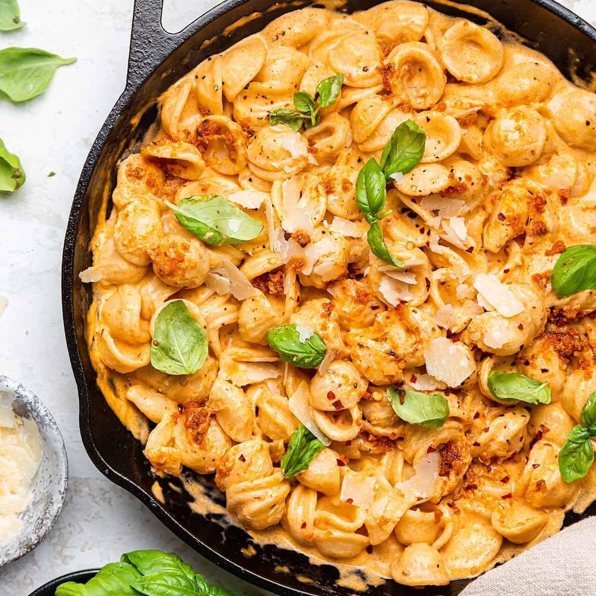 A cast iron skillet filled with creamy, cheesy pasta. The pasta is coated in a rich sauce and topped with fresh basil leaves and grated cheese.