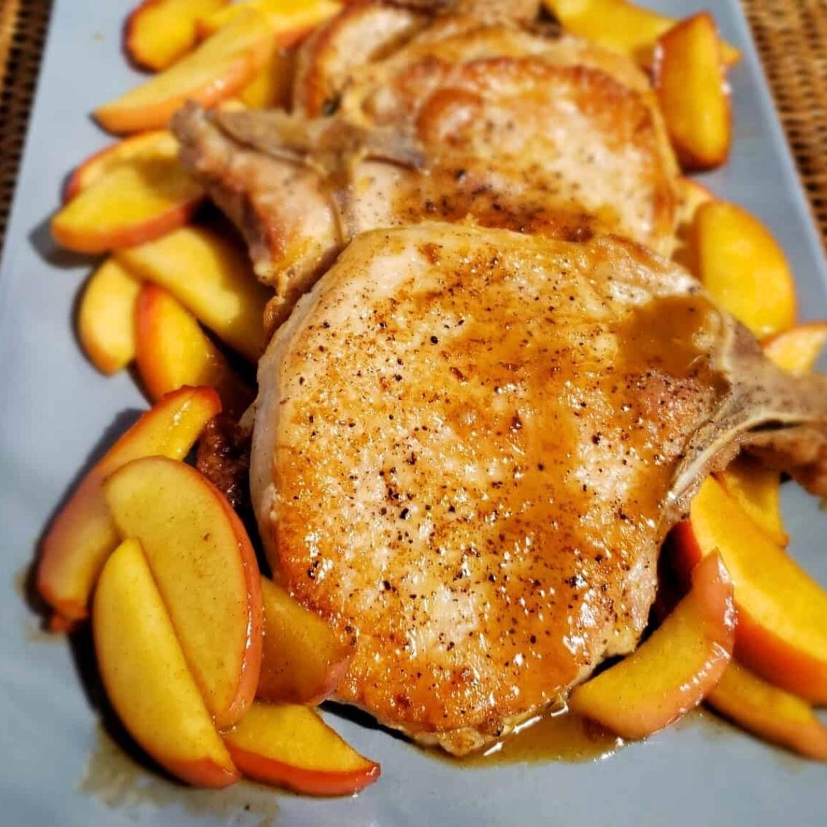 A plate of juicy pork chops served with pan-seared apple slices and a drizzle of sauce. The pork chops look golden brown and crispy, while the apples are caramelized and tender.