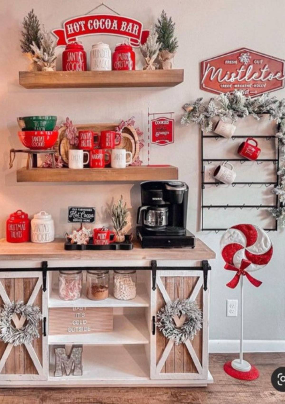 A festive hot cocoa bar with a variety of mugs, candy canes, and other decorations. There is also a coffee maker and a sign that says "Mistletoe”.