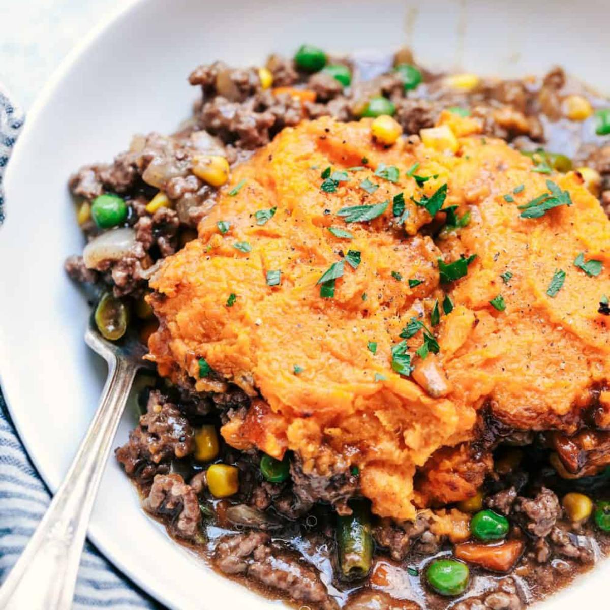 A bowl of shepherd's pie topped with mashed sweet potatoes and garnished with parsley.