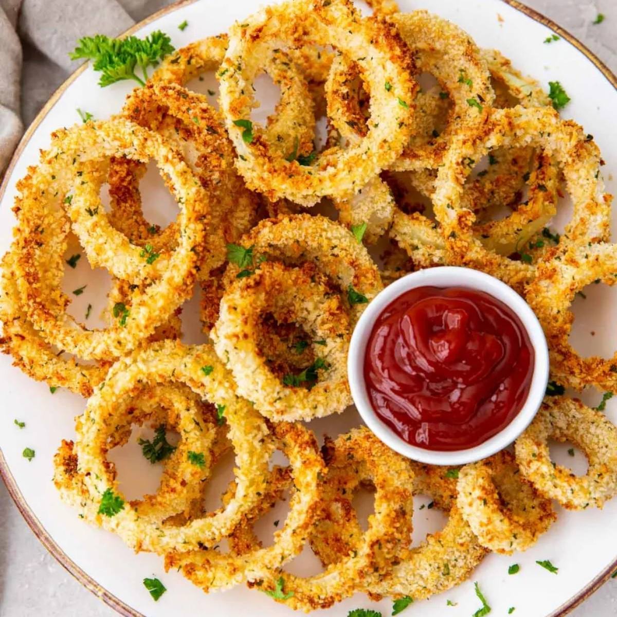 The image shows a plate of crispy, golden onion rings with a small bowl of ketchup on the side. They look delicious!