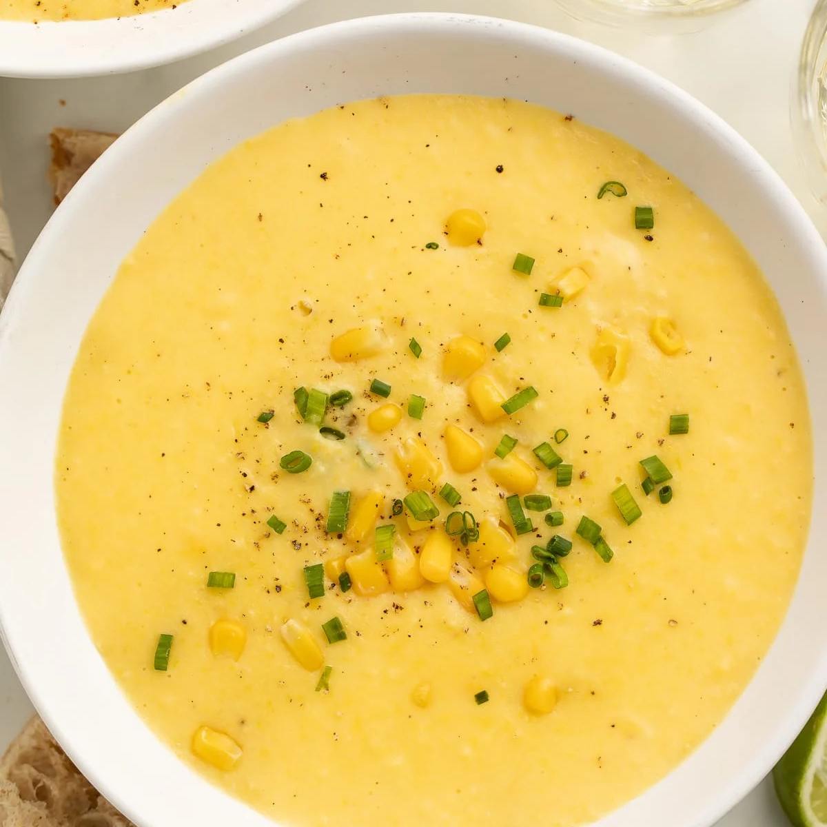 A bowl of creamy, golden corn chowder garnished with fresh corn kernels, chives, and a sprinkle of black pepper.