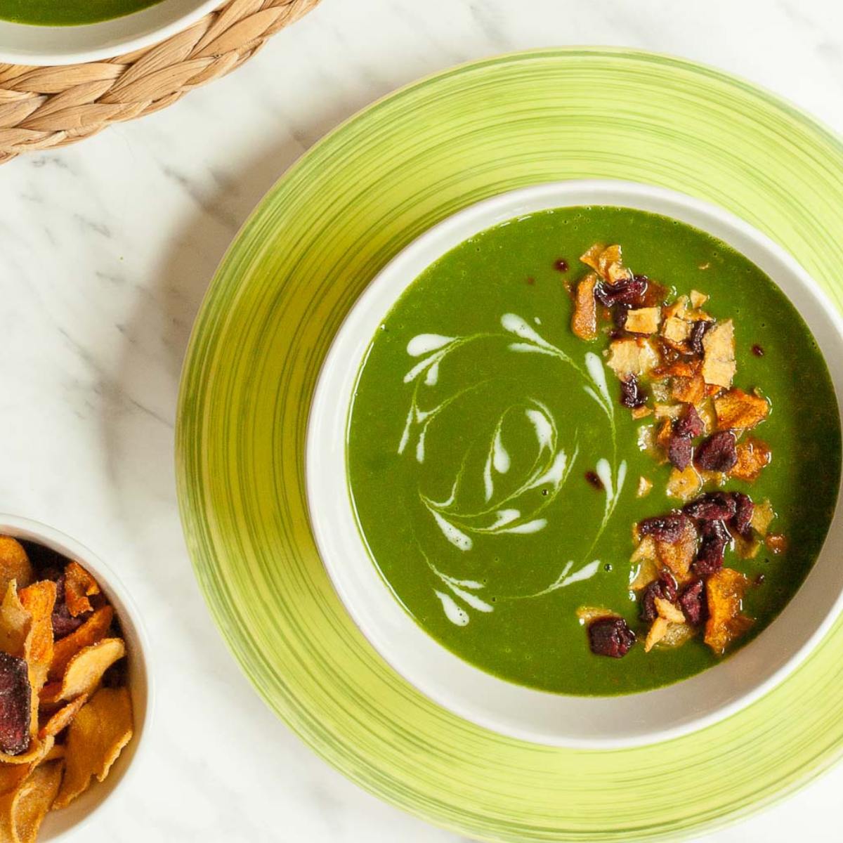 A bowl of vibrant green cream of spinach soup garnished with swirls of cream, crispy bacon bits, and dried cranberries. 