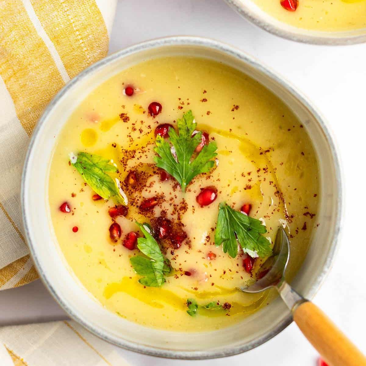 A bowl of creamy, pale green soup garnished with a drizzle of olive oil, black pepper, and fresh herbs. 