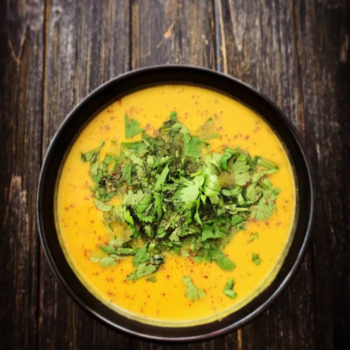 A bowl of creamy, golden soup garnished with fresh cilantro and a sprinkle of red pepper flakes.