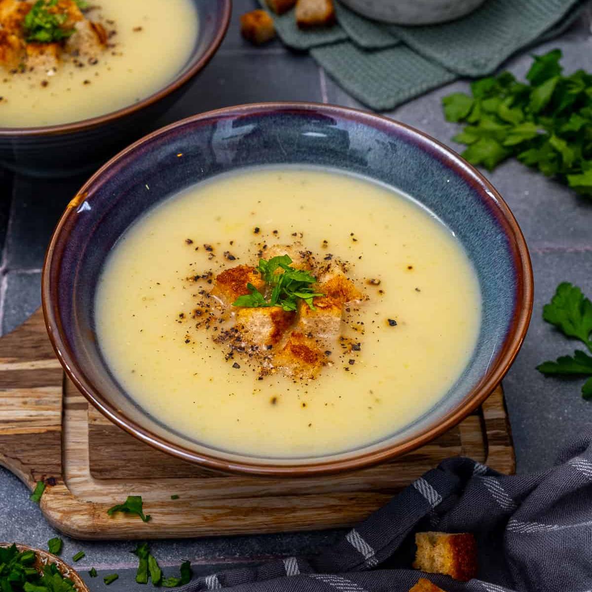 A bowl of creamy, pale yellow soup garnished with croutons, parsley, and a sprinkle of black pepper. 