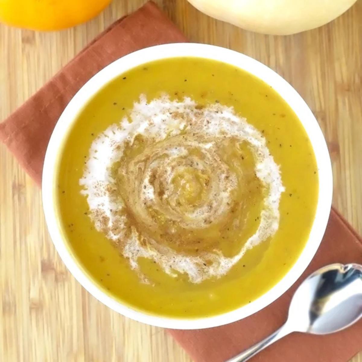 A bowl of creamy, golden pumpkin soup garnished with a swirl of cream and a sprinkle of cinnamon.