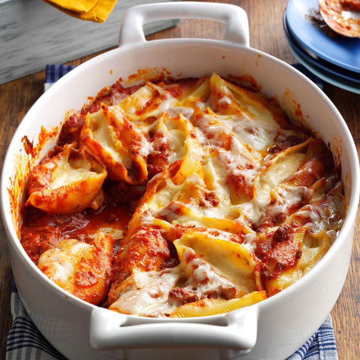 Jumbo pasta shells filled with ricotta, covered in tomato sauce, topped with melted cheese. Baked and served in a white casserole dish.
