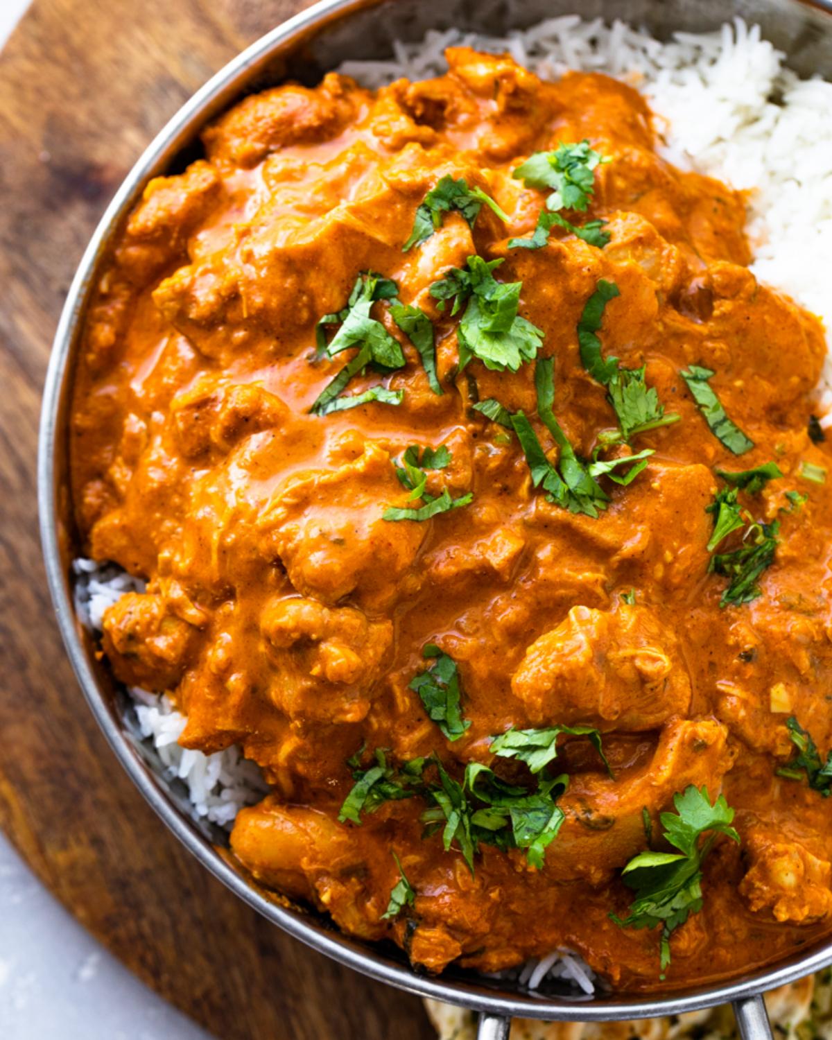 A metal bowl of creamy orange butter chicken served over white rice and garnished with fresh cilantro