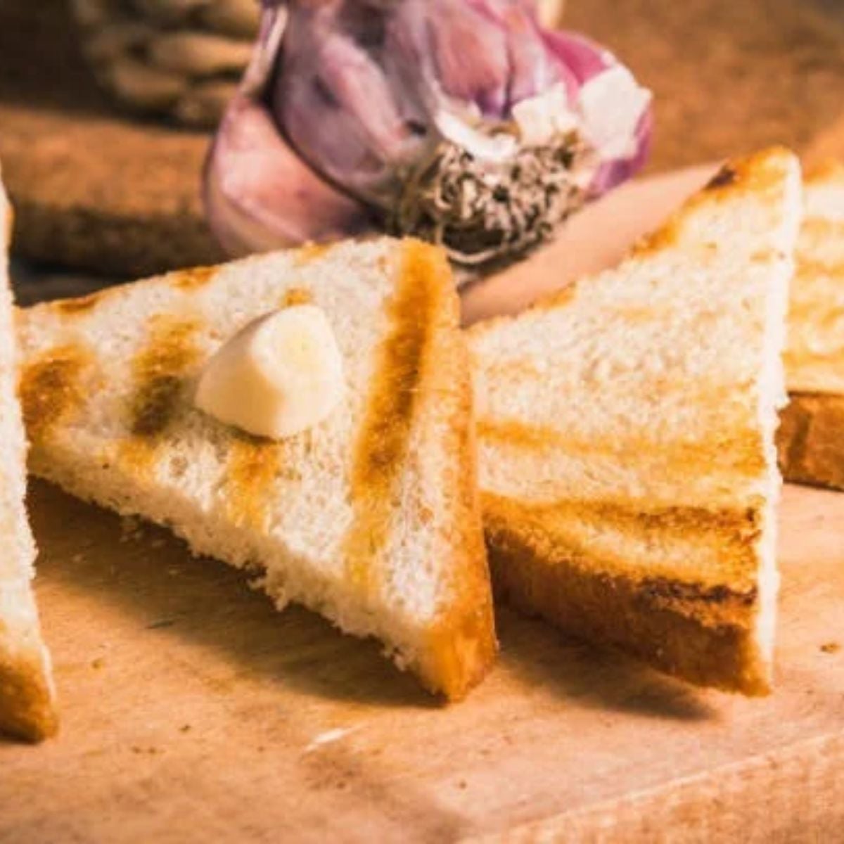 Toast triangles cooling on a wooden table with a blob of butter on the one slice